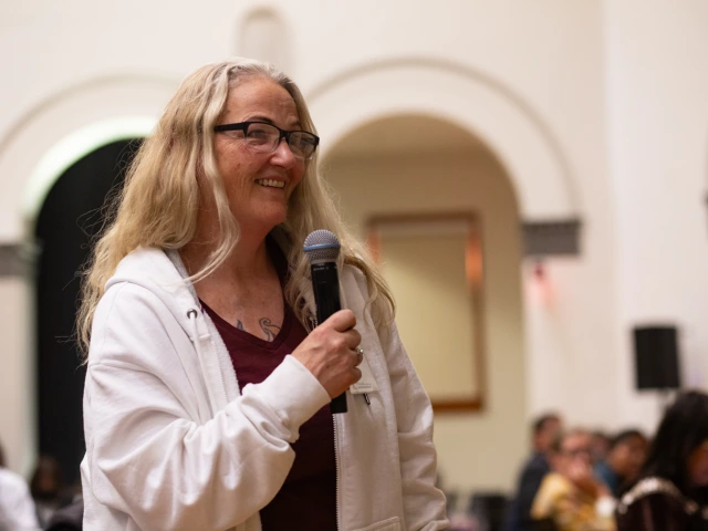 woman in white sweatshirt speaking into a microphone